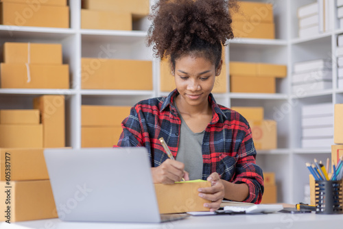 African American female fashion seller using computer checking ecommerce clothing store orders.young business woman entrepreneur working on laptop preparing SME online shipping delivery parcels boxes.