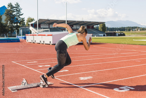 Young woman training for run race start on a stadium track outside