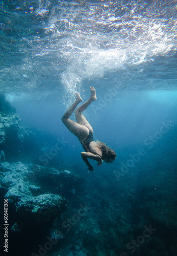 Beautiful girl diving underwater through rocks with sun rays entering the water