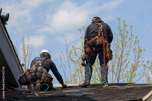 two mans fixing asphalt shingles working on a roof with security rope