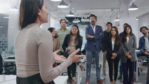 A young Indian Asian female confident entrepreneur or businesswoman passing on a project brief or communicating in a group meeting with employees or team members in a modern corporate office start up