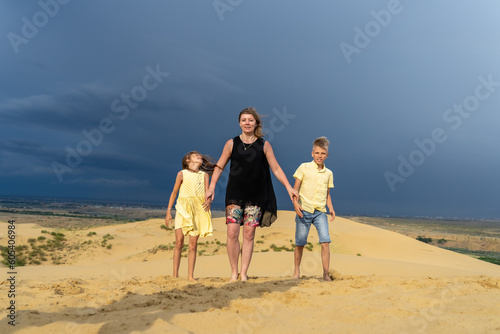 Cheerful mom, son and daughter are standing toghether at desert sand dune in mountains. Fun happy lifestyle in summer