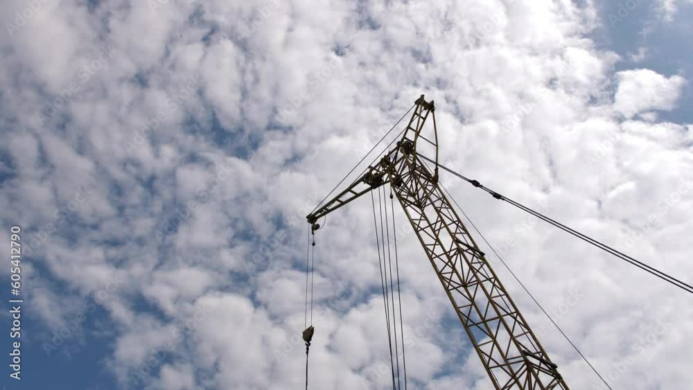 A large industrial crane against a blue sky with lush clouds. Crane at a manufacturing plant. A large industrial crane against a blue sky with lush clouds. Crane at a manufacturing plant.