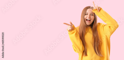 Tablou pe pânză Laughing young woman showing loser gesture on pink background with space for tex