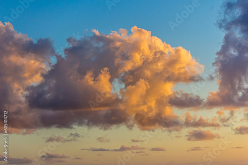 Fluffy cumulus clouds in the sky lit by the sun at sunset or dawn. Landscape in the golden hour, morning or evening, winter or summer. Blue and yellow gradient in the sky. © DmitriiK