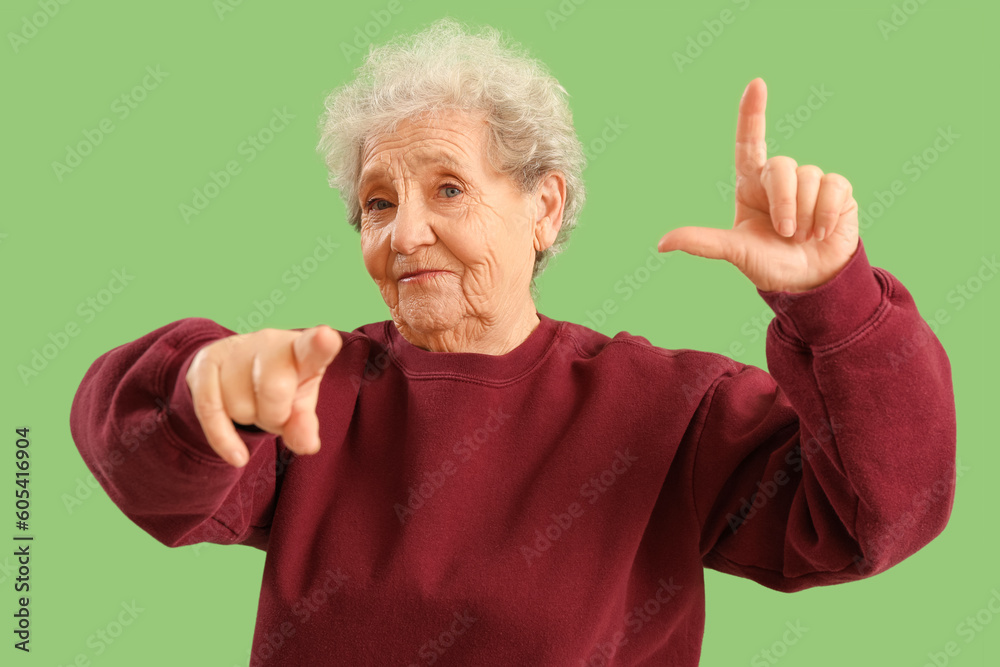 Senior woman showing loser gesture on green background Senior woman showing loser gesture on green background