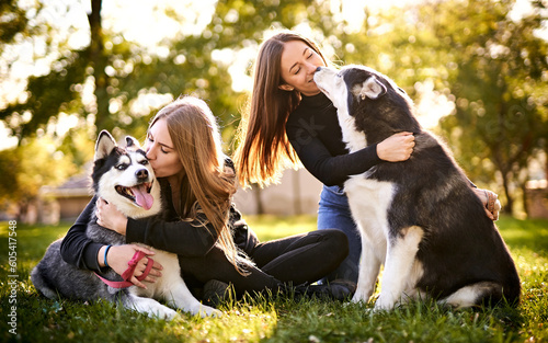 Millennial girls playing with their siberian husky dogs outdoors in the grass - Cheerful young owners and their pets having fun together in the garden - Dog and human frinedship concept