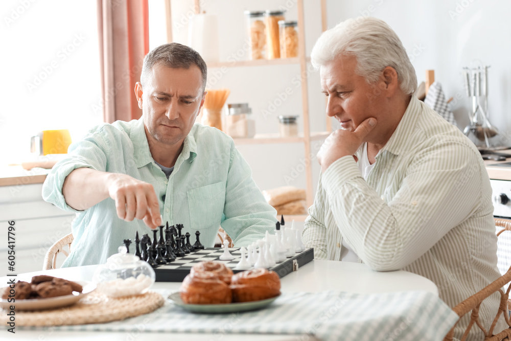 Mature brothers playing chess at table in kitchen