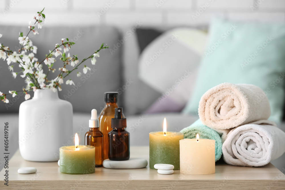 Burning candles, bath supplies, vase with blooming tree branches and rolled towels on table Burning candles, bath supplies, vase with blooming tree branches and rolled towels on table