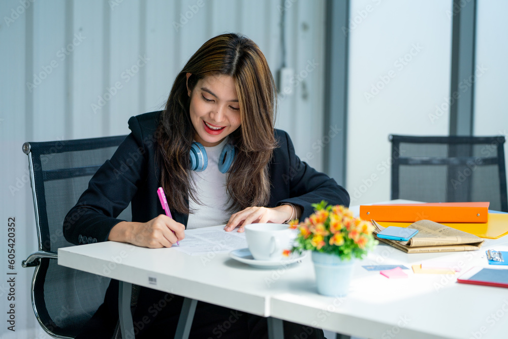 Close up pretty young business woman use pen to write and note on paper in office with happy emotion. Close up pretty young business woman use pen to write and note on paper in office with happy emotion.