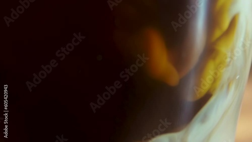 Close-up process of making latte, cappuccino, pouring milk, cream into transparent glass cup with coffee. Abstract brown background. Mixing of liquids. Hot caffeine drinks.