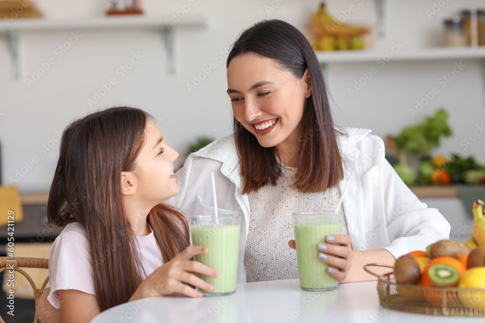Little girl with her mother drinking green smoothie at table in kitchen Little girl with her mother drinking green smoothie at table in kitchen