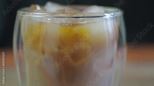 Ice coffee in a tall glass and throwing ice cube from above close up slow motion.Cold summer drink.