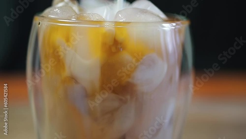 Ice coffee in a tall glass and pouring milk from above on table.Cold summer drink.close up slow motion.