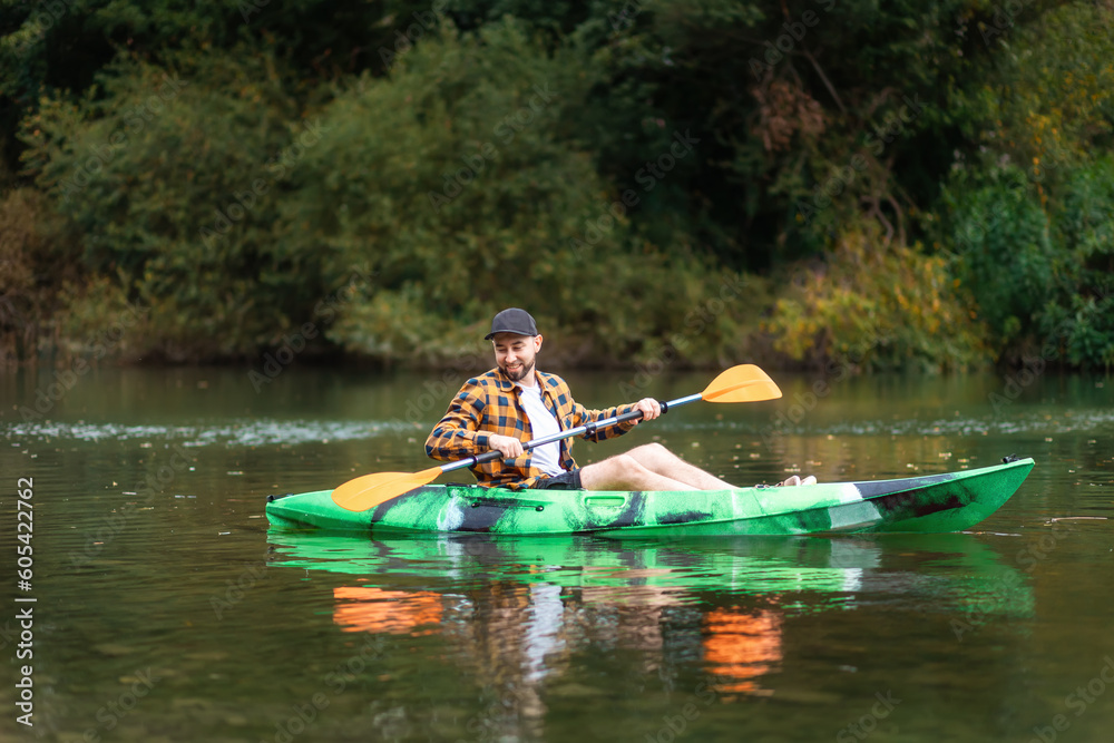 Smiling bearded caucasian man in shirt and cap kayaking at the river. The concept of water sport and activities