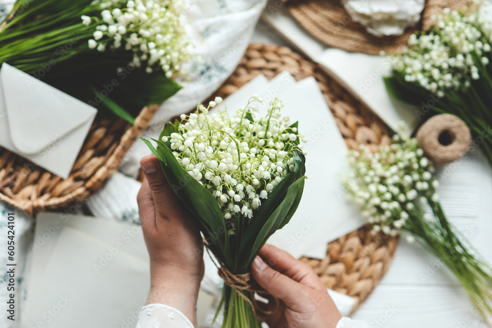 Obraz premium Girl florist holds a bouquet of lilies of the valley in her hands