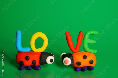 Two toy ladybugs look at each other. Next to the inscription love. Green background. Decorations for Valentine's Day.