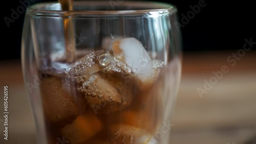 Ice cubes in a tall glass and pouring coffe or tea from above close-up.Cold summer drink.Mixing with red tube