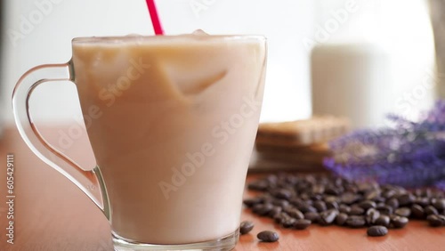Ice coffee in a glass with milk with coffee beans on the table.Cookies and milk bottle. Cold summer drink with red tube