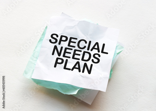 Notebook and pen on a wood table, copy space for text, female hand writing text special needs plan on crumpled yellow paper, work place, brainstorming