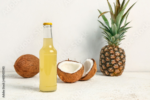 Bottle of fresh soda with coconut and pineapple on light background