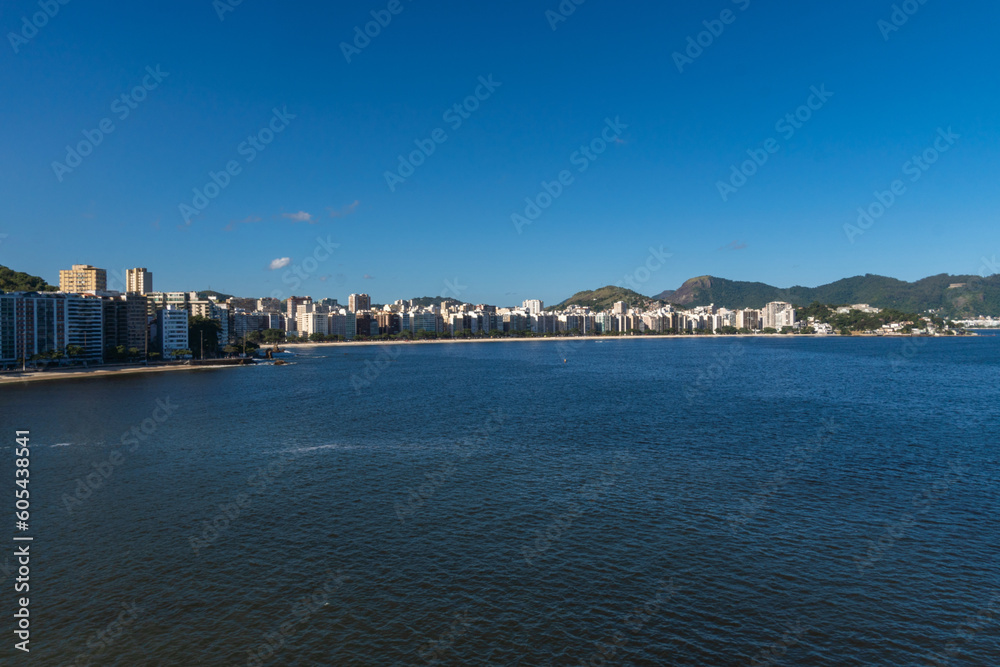 Fototapeta premium View of the edge of Praia de Icaraí, a neighborhood in Niterói, Rio de Janeiro, Brazil. Buildings and houses in front of the beach, surrounded by hills and nature. Bathed by Guanabara Bay. Sunny day