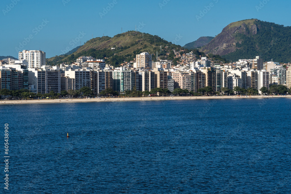 View of the edge of Praia de Icaraí, a neighborhood in Niterói, Rio de Janeiro, Brazil. Buildings and houses in front of the beach, surrounded by hills and nature. Bathed by Guanabara Bay. Sunny day