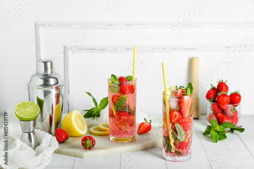 Glass of fresh strawberry mojito with shaker and jigger on white tile table