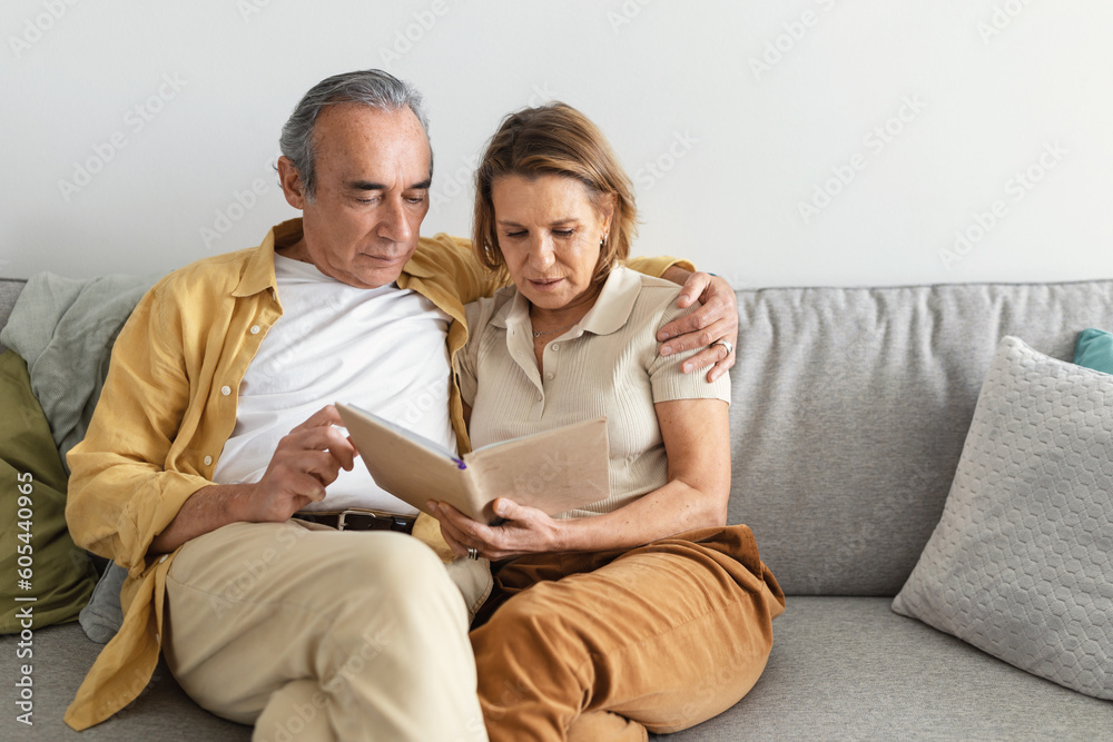 Sweet memories. Happy senior married spouses looking at photo album together, sitting on sofa and having rest at home Sweet memories. Happy senior married spouses looking at photo album together, sitting on sofa and having rest at home