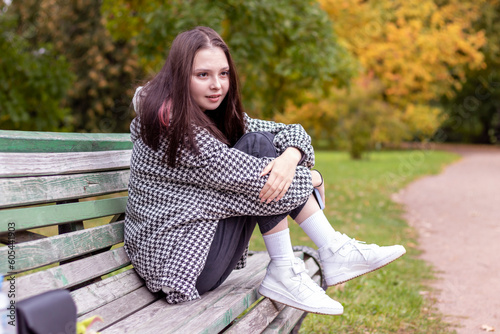 A young woman is sitting with her legs up on an old park bench.