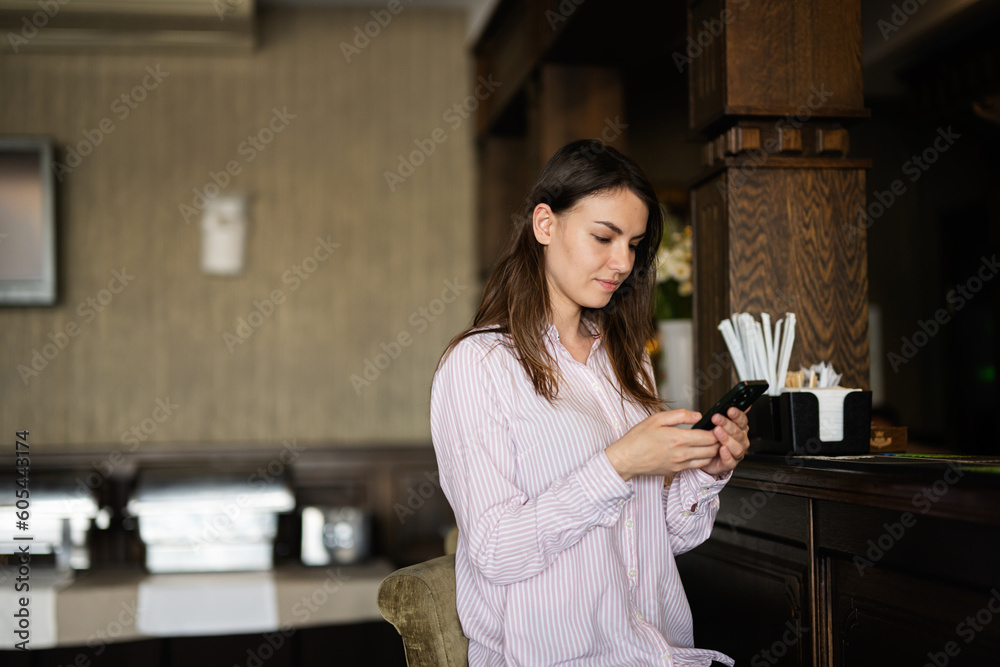 Young beautiful brunette woman sitting near bar counter, waiting for a friend and writing him a text message. Young beautiful brunette woman sitting near bar counter, waiting for a friend and writing him a text message.