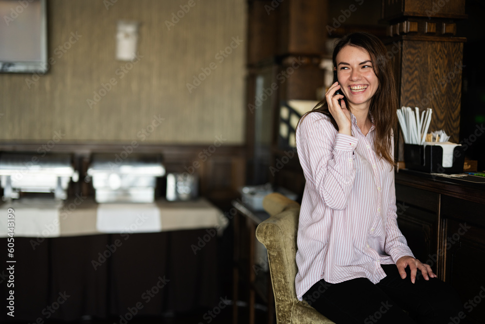 Young beautiful brunette woman sitting near bar counter, talking on the phone and laughing.