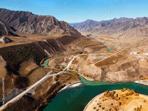 Photos of high mountains from a drone in sunny weather. Top view of the beautiful landscape of the turquoise river, road and forest in autumn