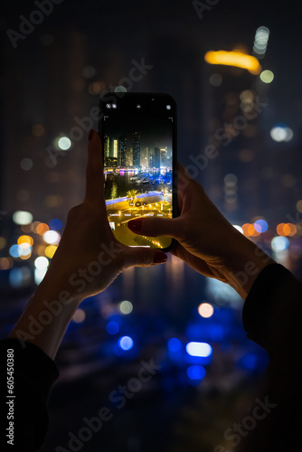 A young woman takes a picture with her mobile phone of the Dubai Marina illuminated at night.