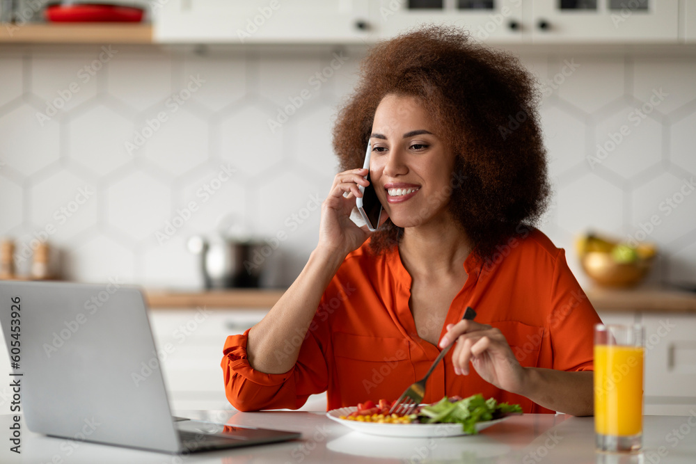 Remote Business. Black Woman Using Cellphone And Working On Laptop In Kitchen Remote Business. Black Woman Using Cellphone And Working On Laptop In Kitchen