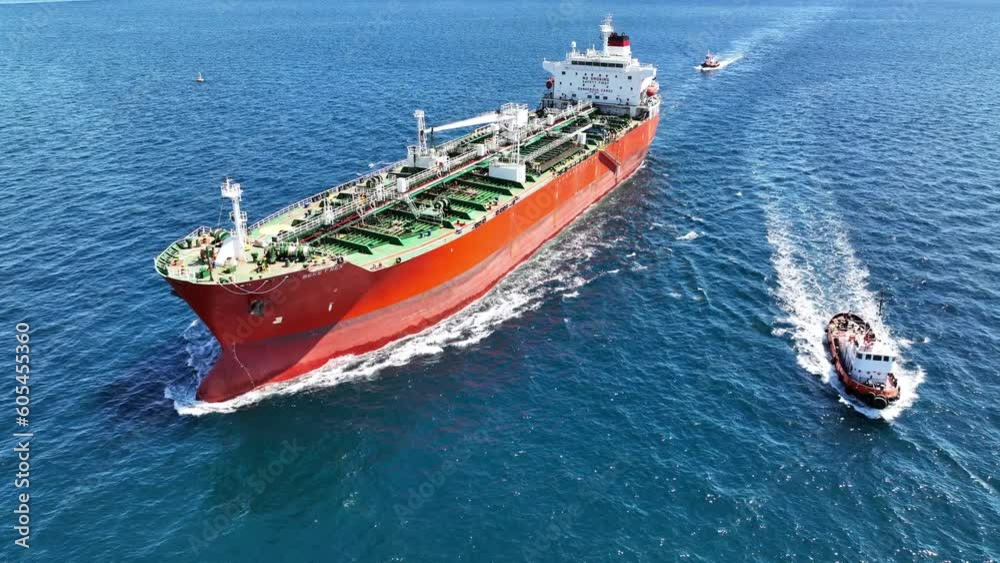 Aerial drone video of huge crude oil tanker assisted by tug boat cruising open ocean deep blue sea Aerial drone video of huge crude oil tanker assisted by tug boat cruising open ocean deep blue sea