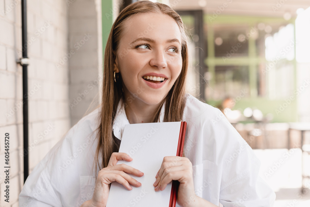 Blonde happy stylish woman with closed book sitting in cafe outside, look at side and dreaming, girl look happy and smiling. Blonde happy stylish woman with closed book sitting in cafe outside, look at side and dreaming, girl look happy and smiling.
