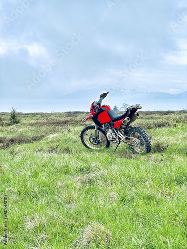 Fototapeta Naklejka Na Ścianę i Meble -  A red motorbike standing a top of a mountain, showcasing the thrilling adventure and triumph of conquering the rugged terrain, surrounded by breathtaking scenic views and the exhilarating sense of