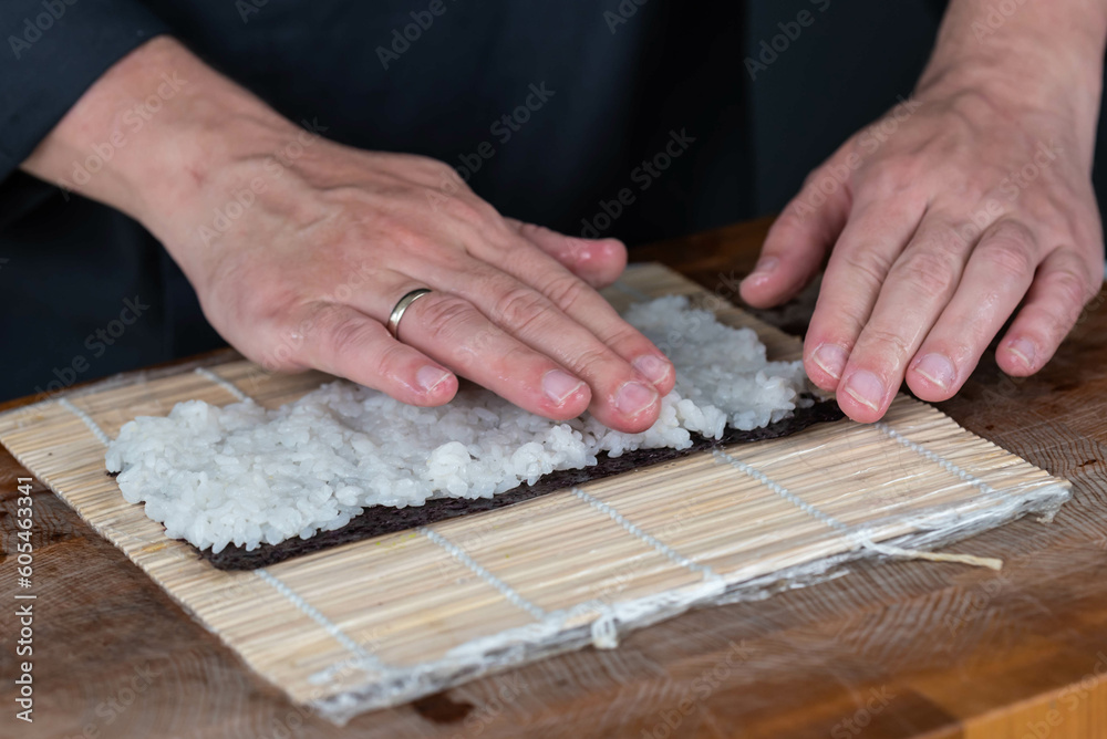 Close up of sushi chef hands preparing japanese food. Man cooking and making rice for sushi at restaurant. Traditional asian seafood rolls on cutting board.