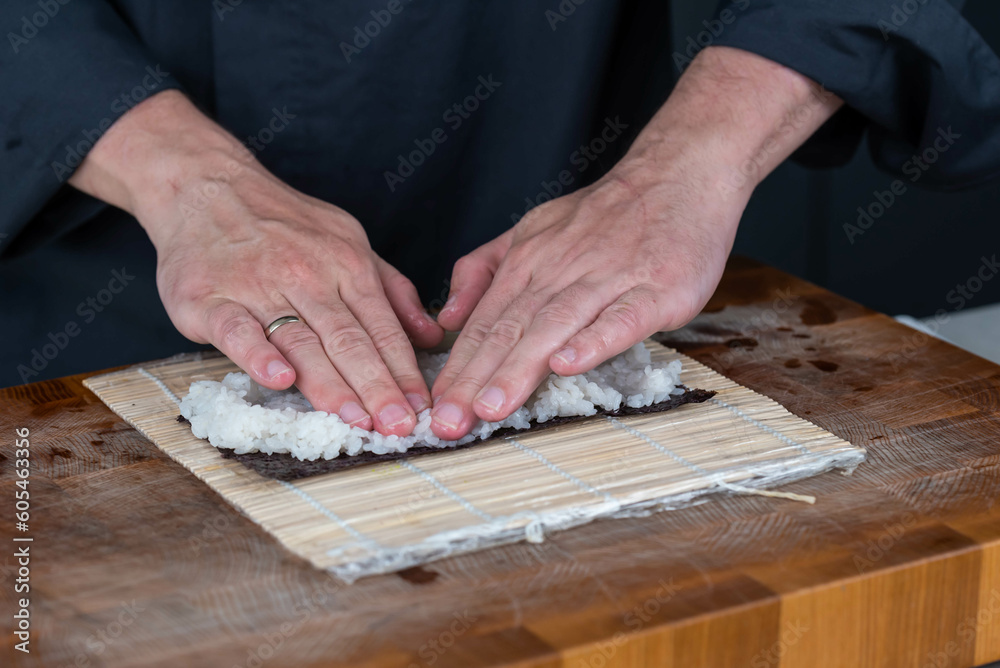 Close up of sushi chef hands preparing japanese food. Man cooking and making rice for sushi at restaurant. Traditional asian seafood rolls on cutting board. Close up of sushi chef hands preparing japanese food. Man cooking and making rice for sushi at restaurant. Traditional asian seafood rolls on cutting board.