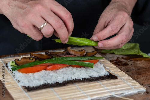 Close up of sushi chef hands preparing japanese food. Man cooking sushi at restaurant. Traditional asian seafood rolls on cutting board.