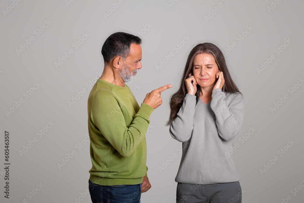 Strict angry caucasian aged husband scolds his wife, lady covers ears Strict angry caucasian aged husband scolds his wife, lady covers ears