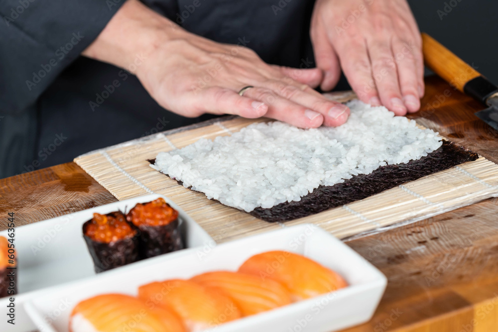 Close up of sushi chef hands preparing japanese food. Man cooking sushi with red caviar and salmon at restaurant. Traditional asian seafood rolls on cutting board.