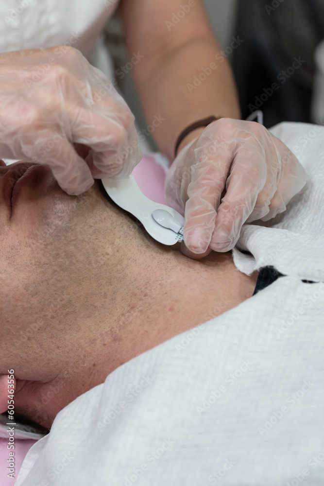 Man at electric facial massage procedure against double chin at cosmetology beauty clinic. Man at electric facial massage procedure against double chin at cosmetology beauty clinic.