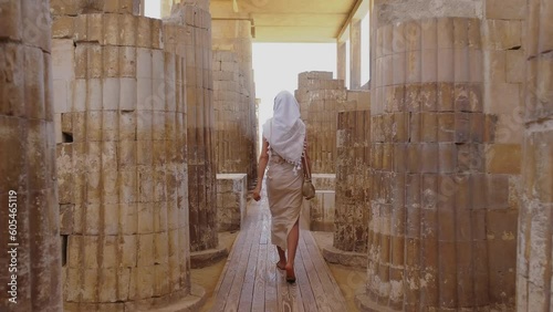 Woman is walking amongst world's oldest known stone columns at Djoser's step pyramid complex.