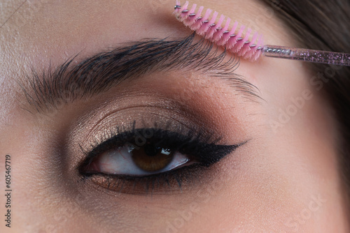 Perfect eyebrows. Close up of woman getting eyebrow make-up. Macro applying cosmetics on her eyebrow with brush. Perfect shape of eyebrow, brown eyeshadows and long eyelashes. Shape eyebrows.