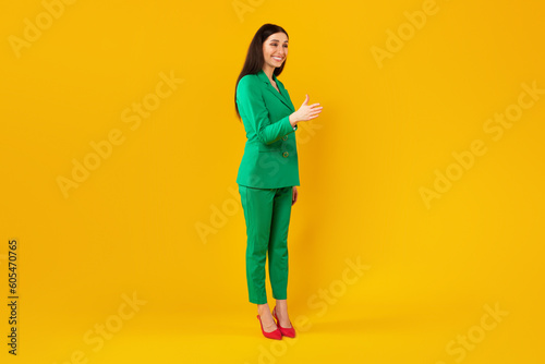 Young stylish woman stretching hand for handshake, greeting and smiling, standing over yellow background, full length © Prostock-studio