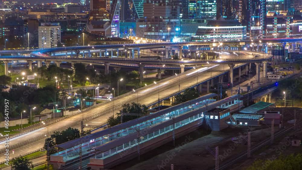 Small Ring of the Moscow Railways night timelapse. Orbital railway route in Moscow, Russia. Shelepikha Station aerial top view with traffic on third transport ring and skyscrapers behind