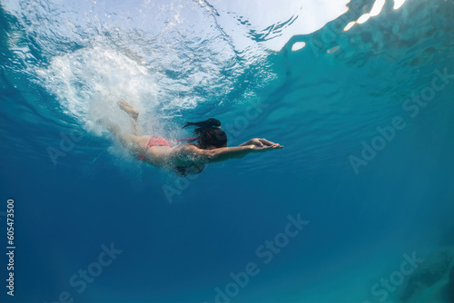 Underwater view of beautiful woman in red bikini jumping from boat into water.