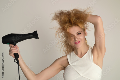 Young woman drying her hair with a hairdryer isolated on studio background. Young woman with blow dryer drying hair, making hairdo. Close up portrait of beautiful young woman in drying hairstyle.